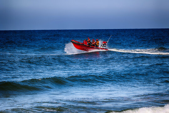 Pomarańczowa ł&oacute;dka z ratownikami płynie z akcją ratowniczą na morzu. 