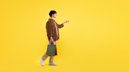 Fototapeta na wymiar Man Carrying Shopping Bags Pointing Finger Aside Over Yellow Background