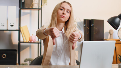 Fototapeta na wymiar Dislike. Upset businesswoman girl working on laptop computer at home office thumbs down sign gesture, expressing discontent, disapproval, dissatisfied bad work. Displeased serious freelancer woman