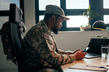 Army officer with cellphone at desk.