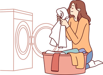Housewife woman sits near washing machine and inhales fragrant smell of freshly washed towel