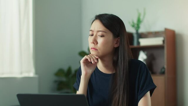 Serious Thoughtful Young Asian woman sit on at desk working at home living room. Asian female remote work using laptop looking around and thinking about problem solution or new business ideas