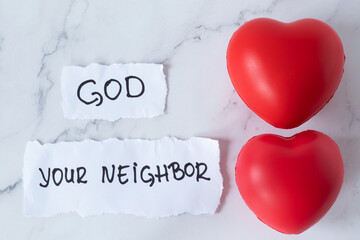 Love God and your neighbor, handwriting on paper with two red hearts on white marble table. Top...