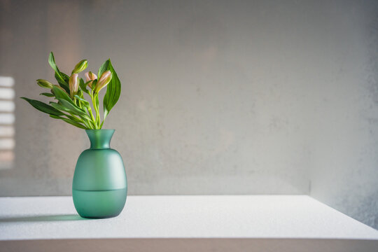 Minimalism style interior decor. Fresh flowers in green glass vase on the natural stone shelf