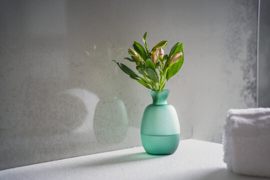 Minimalism style interior decor. Fresh flowers in green glass vase on the natural stone shelf