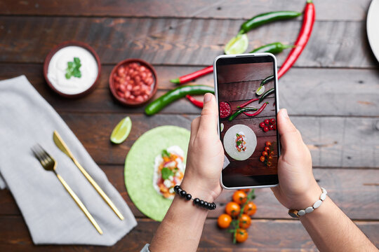Top view of man making photo of food on wooden table on mobile phone for food blog