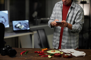 Fototapeta premium Young photographer making photo of still life of food on his smartphone in studio