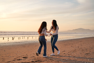 silhouette latina mother and teenage daughter playing enjoying laughing together on the beach shore...