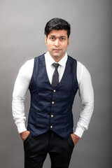 Studio shot of cheerful, young, handsome Indian business man in formal wear against grey background. Male model. Fashion Portrait.