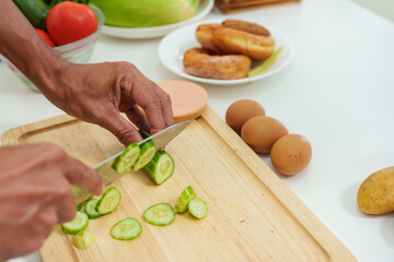 Close-up hand of Asian man using a knife to thinly slice cucumbers. It's a cutting board that sits on the kitchen table. to prepare sandwiches for breakfast On days when have work at home alone