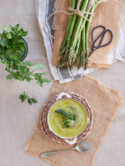 green asparagus cream soup served in a bowl at the table beside a bunch of fresh wild asparagus and parsley.