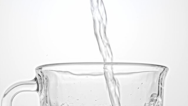 Water pouring into glass on white  background, close up. Fresh pure drinking water splashing in glass while pouring, creating bubbles, slow motion