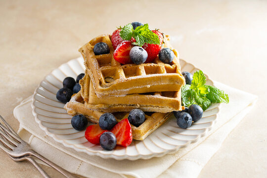Belgian homemade waffles with strawberries, blueberries and powder sugar. 