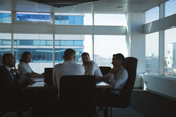 Silhouettes of people sitting at the table. Team of young business people working and communicating together in a modern office. Corporate team and manager in a meeting