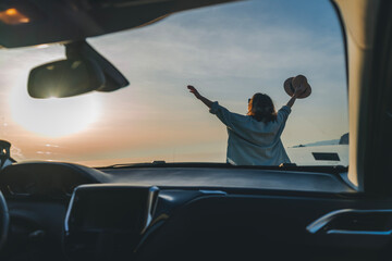 Happy woman cheerful raising her hands up and feeling happiness, Happy cheerful young woman traveling on the sea by car. At sunset