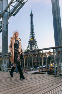 Stylish smiling woman in cap walking on bridge