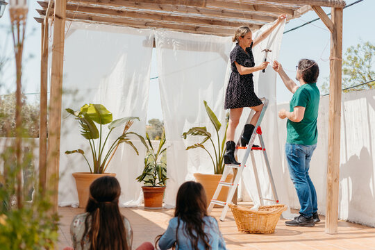 Couple placing curtains on pergola at terrace