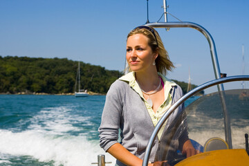A beautiful young woman driving her powerboat around a mediterranean coastline