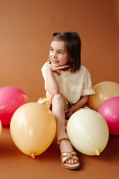 Portrait of kid in studio with colored balloons and brown backdrop