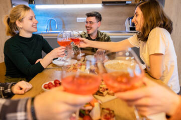 Group of friends enjoying dinner. Focus on hands having a toast with rose wine.