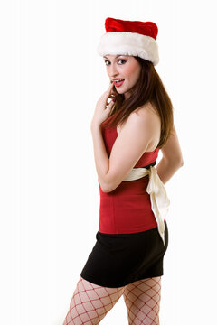 Attractive long haired brunette woman wearing sexy red and black top and short black skirt and santa hat and red fishnet stocking with a happy expression standing on white