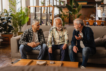 three old friends chatting on sofa at home, meeting of senior men with gray hair having fun indoors.