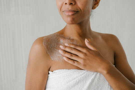 Calm woman in towel applying clay mask on body