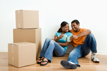 Fototapeta na wymiar African American male and female couple sitting on floor next to moving boxes relaxing.