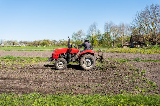 A red tractor on which a farmer sits and cultivates the land for further planting and sowing.