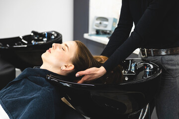 Master woman hairdresser gently washes the girl's hair with shampoo and conditioner before styling in a beauty salon.