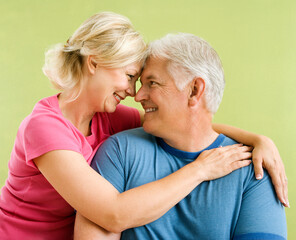 Portrait of smiling middle-aged couple in front of green wall snuggling.