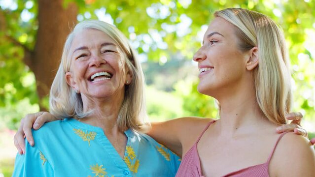 Portrait of multi-generation family with senior mother and adult daughter standing outside in garden, park or countryside laughing together- shot in slow motion
