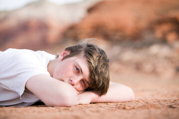 Obraz na płótnie Canvas teenager male laying on the ground outdoors, natural light with mountains in background