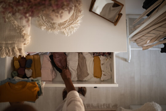 Black woman putting newborn apparel into dresser