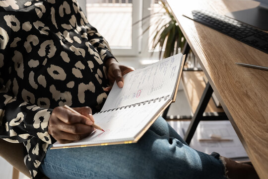Crop pregnant woman circling notes in notebook