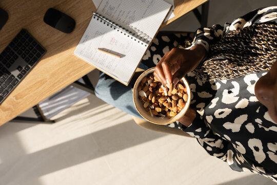 Crop black woman eating nuts at workplace