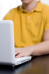 Young man in yellow shirt types on notebook (shallow DOF, focus on lid)