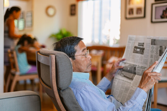 Senior man reading newspaper at home by family