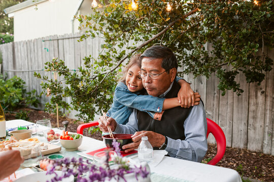 Granddaughter hugs her grandfather eating at garden