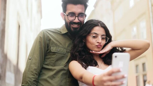 Portrait of young indian couple grimacing taking selfie photograph saving great memories on smartphone mobile phone at city centre Happy relationship concept
