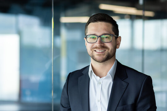Close-up photo. Portrait of a young businessman, founder, director in a suit and glasses standing in the office and smiling at the camera