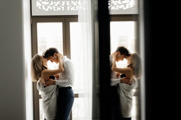 Cheerful couple in love kissing  near window in hotel room
