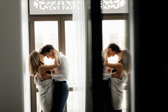Cheerful couple in love kissing  near window in hotel room
