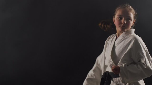 Young karate girl wearing kimono and posing against black background with smoke