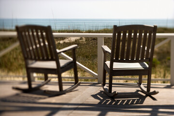 Two wooden rocking chairs sitting on a deck. They are facing the shore. Horizontal shot.