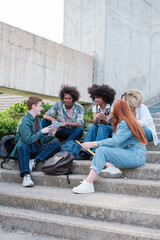 Group of university students sitting on some stairs of the college in the open air. Concept: education, friendship, together