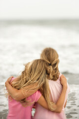 Rear view of a mother and daughter embracing at the beach. Vertical shot.