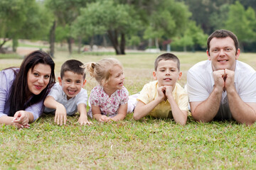 Fototapeta premium Cheerful family of five lying on lawn in the green park and looking at you