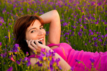 Beautiful young woman lying on the nature and talking at cellphone