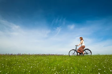 Tuinposter Happy young woman on a green meadow riding a bicycle © Designpics